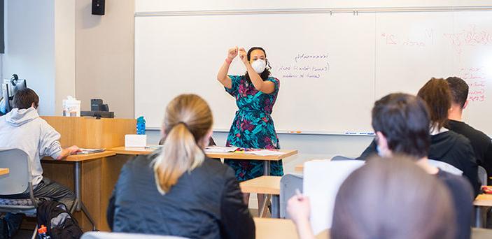 Professor Allyson Ferrante teaches in front of a white board with a definition of "irrevocably" written on it as students look on