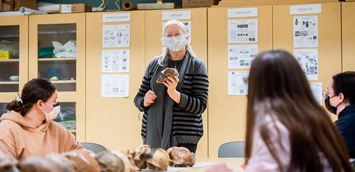 北达科他州立大学教授埃伦·英格曼森(艾伦Ingmanson)在一张桌子的前面讲课时，手里拿着一个头骨，桌子上放着一排头骨，学生们围坐在桌边听着，做着笔记